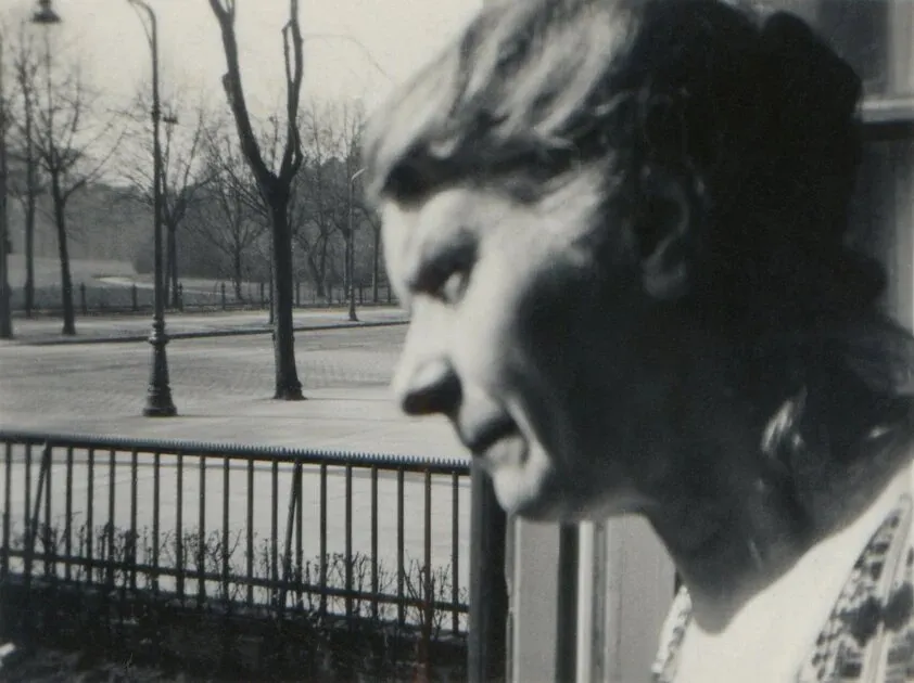 Fotografie alb-negru: o persoană vârstnică din profil, lângă gardul unui parc